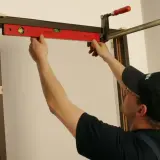 Majster sprawdza poziomem, jak zakryć metalowe futryny, używając zacisku do stabilizacji.