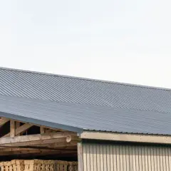 Szeroki dach z blachy trapezowej, chroniący drewnianą konstrukcję i składowane materiały.