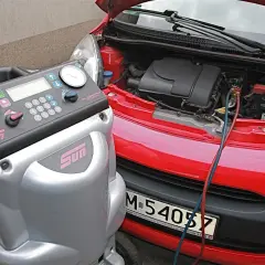 Urządzenie do serwisu klimatyzacji podłączone do czerwonego samochodu. Dowiedz się, ile kosztuje nabicie klimatyzacji.
