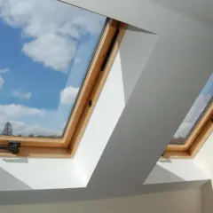 Dwa drewniane okienka w dachu ukazują błękitne niebo z białymi chmurami.