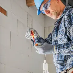 Elektryk w kasku i okularach montuje oprawkę żarówki. Ciekawe, ile za punkt elektryczny zapłacę za taką pracę.