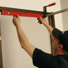 Majster sprawdza poziomem, jak zakryć metalowe futryny, używając zacisku do stabilizacji.