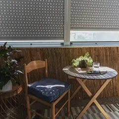 Przytulna loggia z balkonem, gdzie stoi drewniane krzesło z poduszką, okrągły stolik z napojem i roślinami.