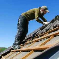 Pracownik układa dachówki na dachu dwuspadowym. Szacowany koszt dachu dwuspadowego 200m2.