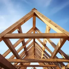 Drewniana konstrukcja nośna dachu, widok od dołu na tle błękitnego nieba.
