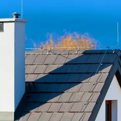 Biały komin i dachówka na tle błękitnego nieba. Na dachu widoczny jest piorunochron, chroniący dom przed burzą.