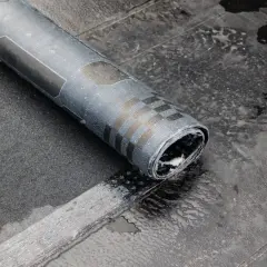 Zrolowana papa na zimno, z charakterystycznym wzorem, leży na mokrej, ciemnej powierzchni.