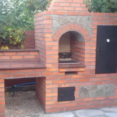 Solidny grill z cegły szamotowej, z kamiennym łukiem nad paleniskiem i metalowymi drzwiczkami. Idealny do ogrodu.