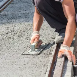 Robotnik w rękawiczkach wygładza świeży, mokry beton kielnią. Powierzchnia jest jeszcze wilgotna, ale wkrótce stanie się suchy beton.