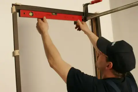 Majster sprawdza poziomem, jak zakryć metalowe futryny, używając zacisku do stabilizacji.