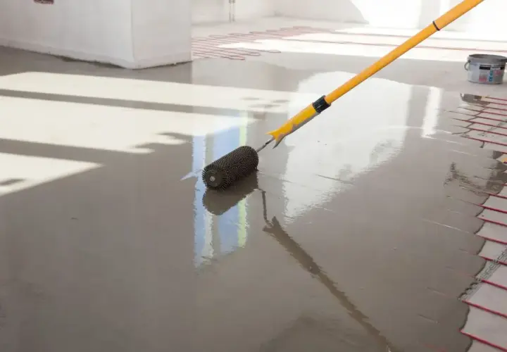 Wałek do betonu z kolcami rozprowadza świeży wylewany **anhydryt** na podłodze z ogrzewaniem podłogowym.