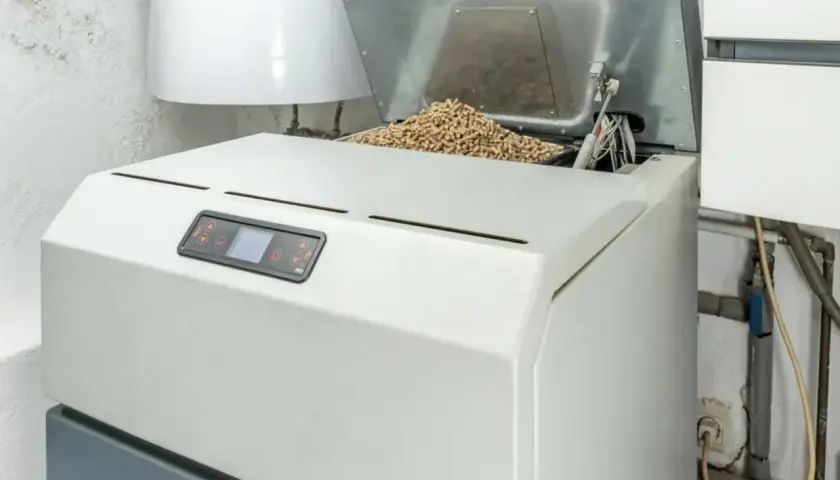 Kocioł na paliwo stałe z zasobnikiem pełnym pelletu. Obok bojler i instalacja grzewcza.