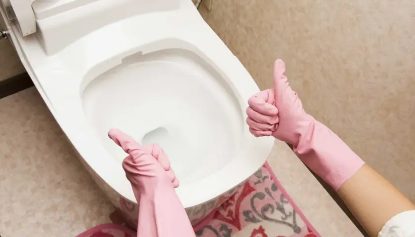 Ręce w różowych rękawiczkach pokazują kciuk w górę i wskazują na toaletę. Proste wskazówki, jak odetkać toaletę, gdy masz problem.
