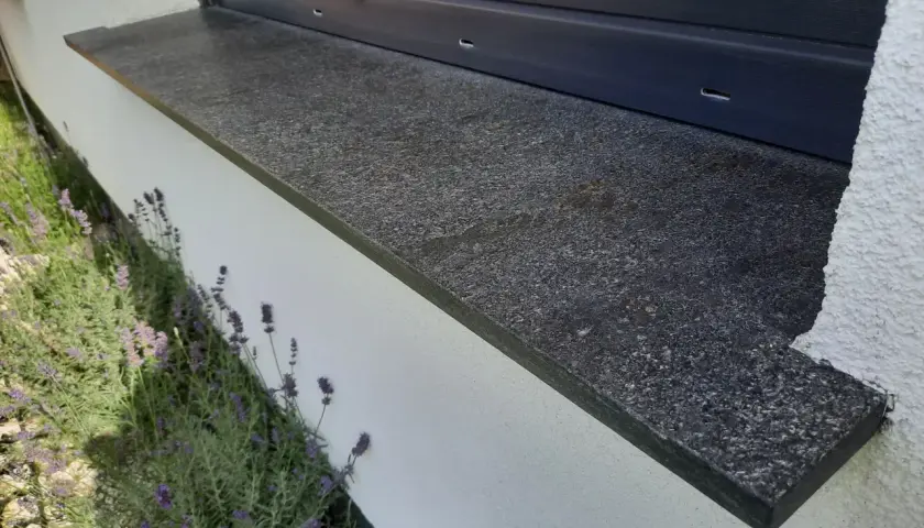 Granitowy parapet zewnętrzny wystaje ok. 5 cm od ściany, chroniąc ją przed deszczem. Obok kwitnie lawenda.