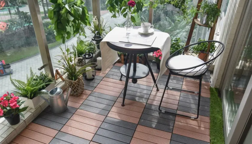 Czym wyłożyć balkon? Drewnopodobne płytki tarasowe w kolorze brązowym i szarym tworzą przytulną przestrzeń z roślinami i meblami.