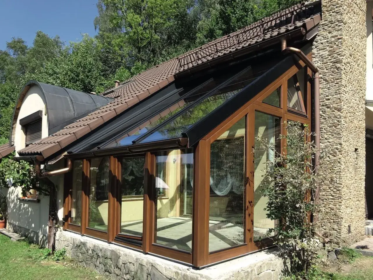 Nowoczesny ogród zimowy na tarasie, z drewnianymi ramami i przeszklonym dachem, idealny do relaksu przez cały rok.