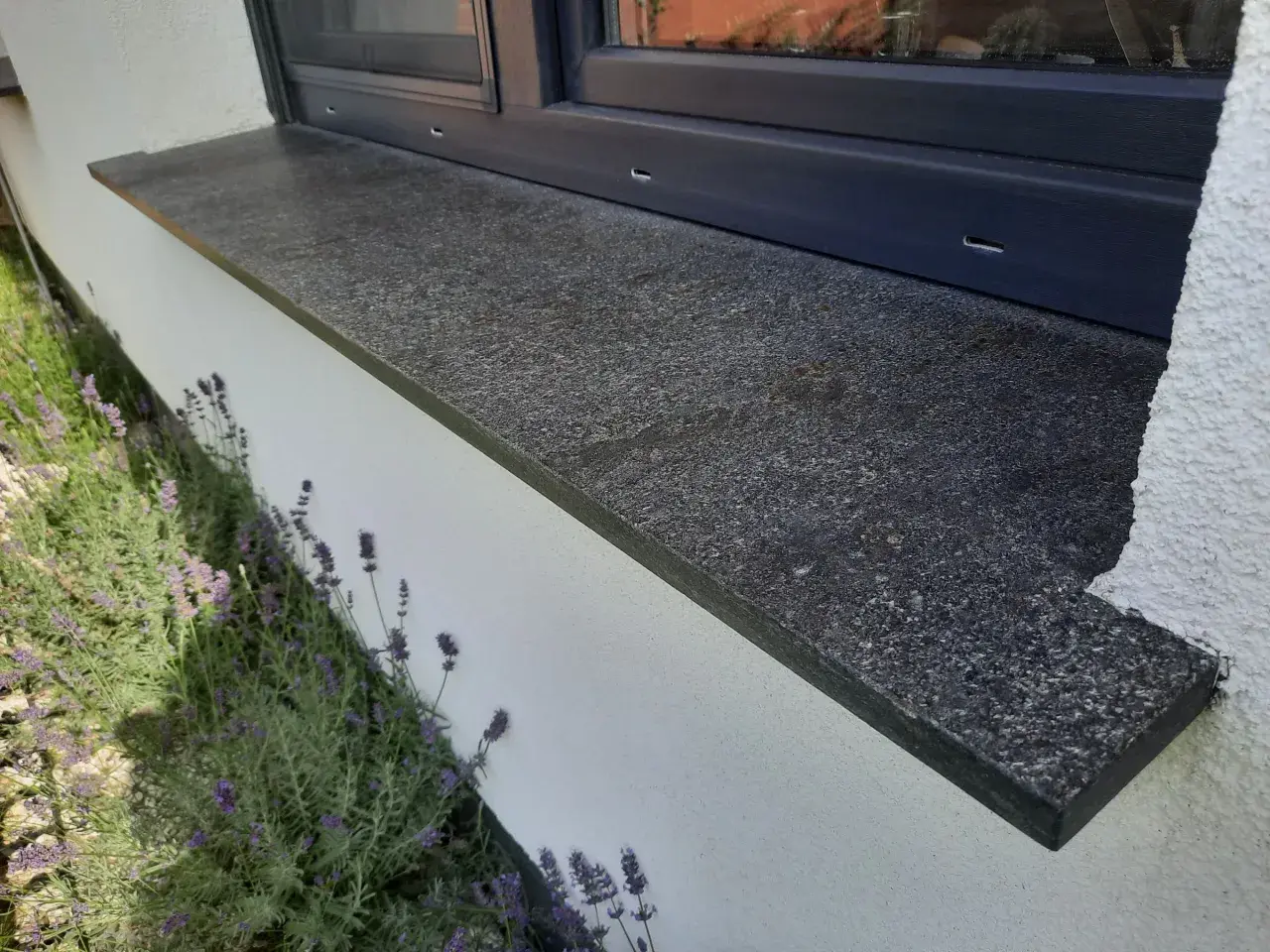 Granitowy parapet zewnętrzny wystaje ok. 5 cm od ściany, chroniąc ją przed deszczem. Obok kwitnie lawenda.