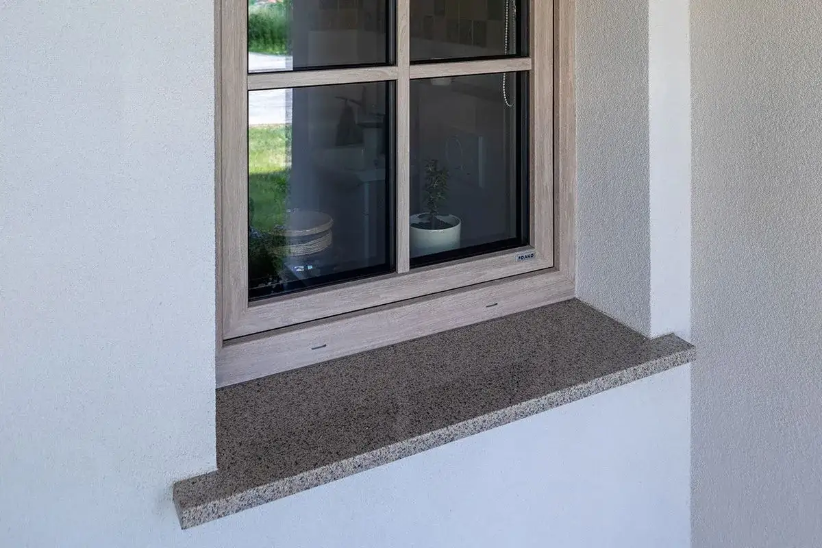 Kamienny parapet to stylowe i praktyczne rozwiązanie, czym obrobić okna z zewnątrz. Elegancko komponuje się z jasną elewacją.