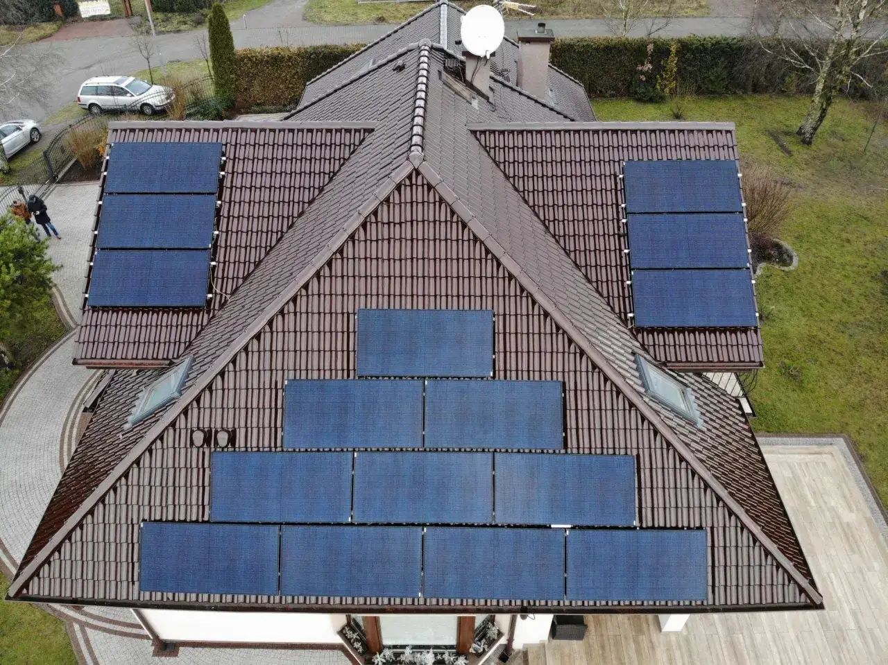 Montaż paneli fotowoltaicznych na brązowym dachu domu. Widać kilka rzędów ciemnoniebieskich paneli, które zbierają energię słoneczną.