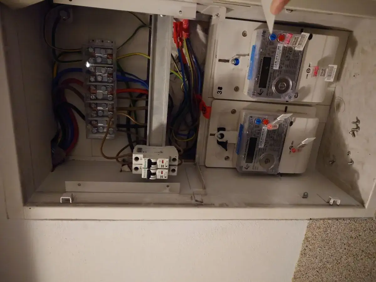 W skrzynce elektrycznej widać dwa liczniki energii elektrycznej, przewody i bezpieczniki.