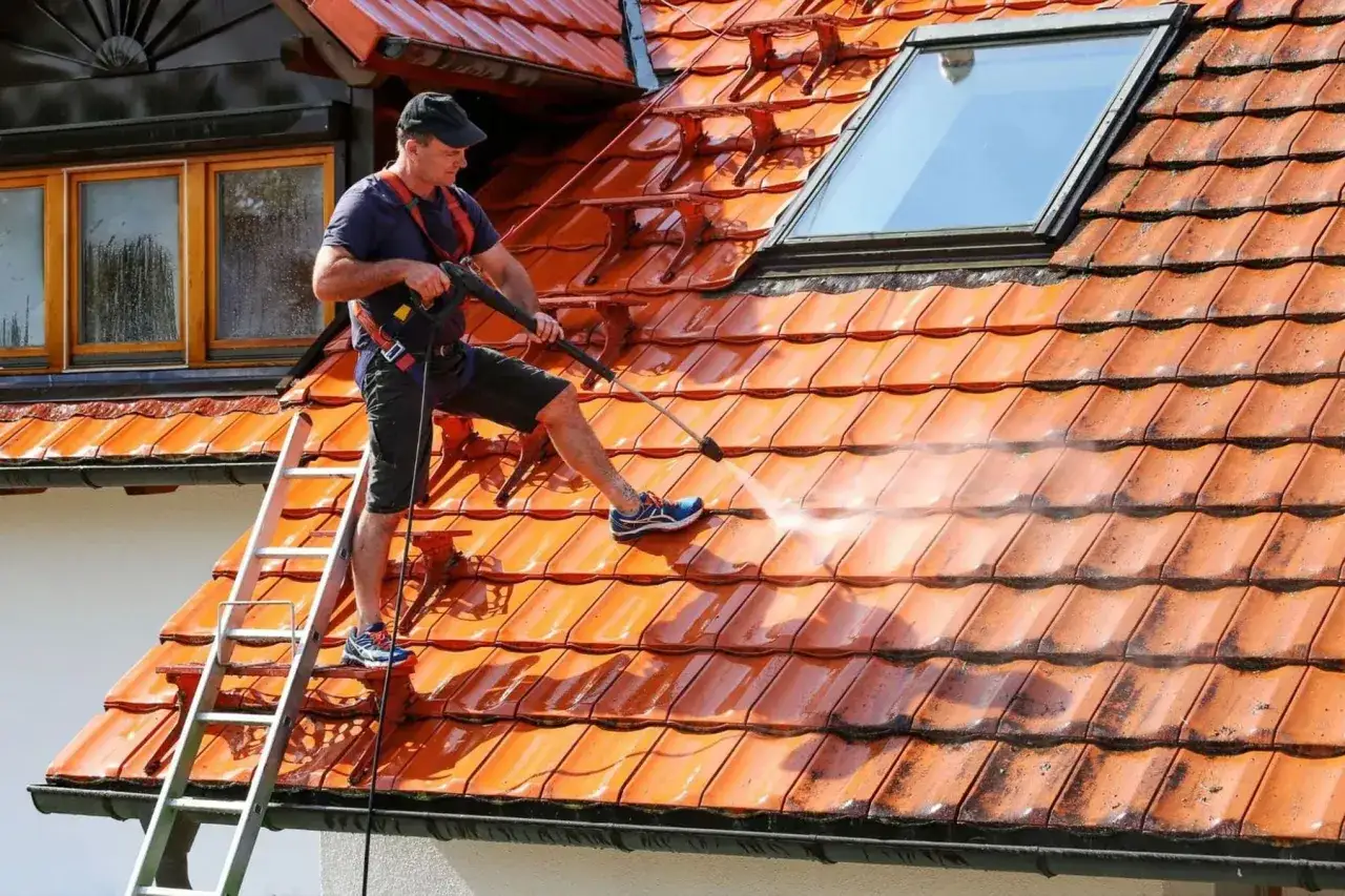 Mężczyzna na drabinie myje dach Karcherem. Sprawdź, jaka jest mycie dachu Karcherem cena i odzyskaj blask swojego domu!