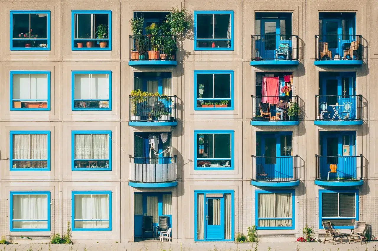 Elegancka loggia i balkon z niebieskimi ramami okiennymi, pełne zieleni i suszącego się prania, tworzą barwną fasadę bloku.