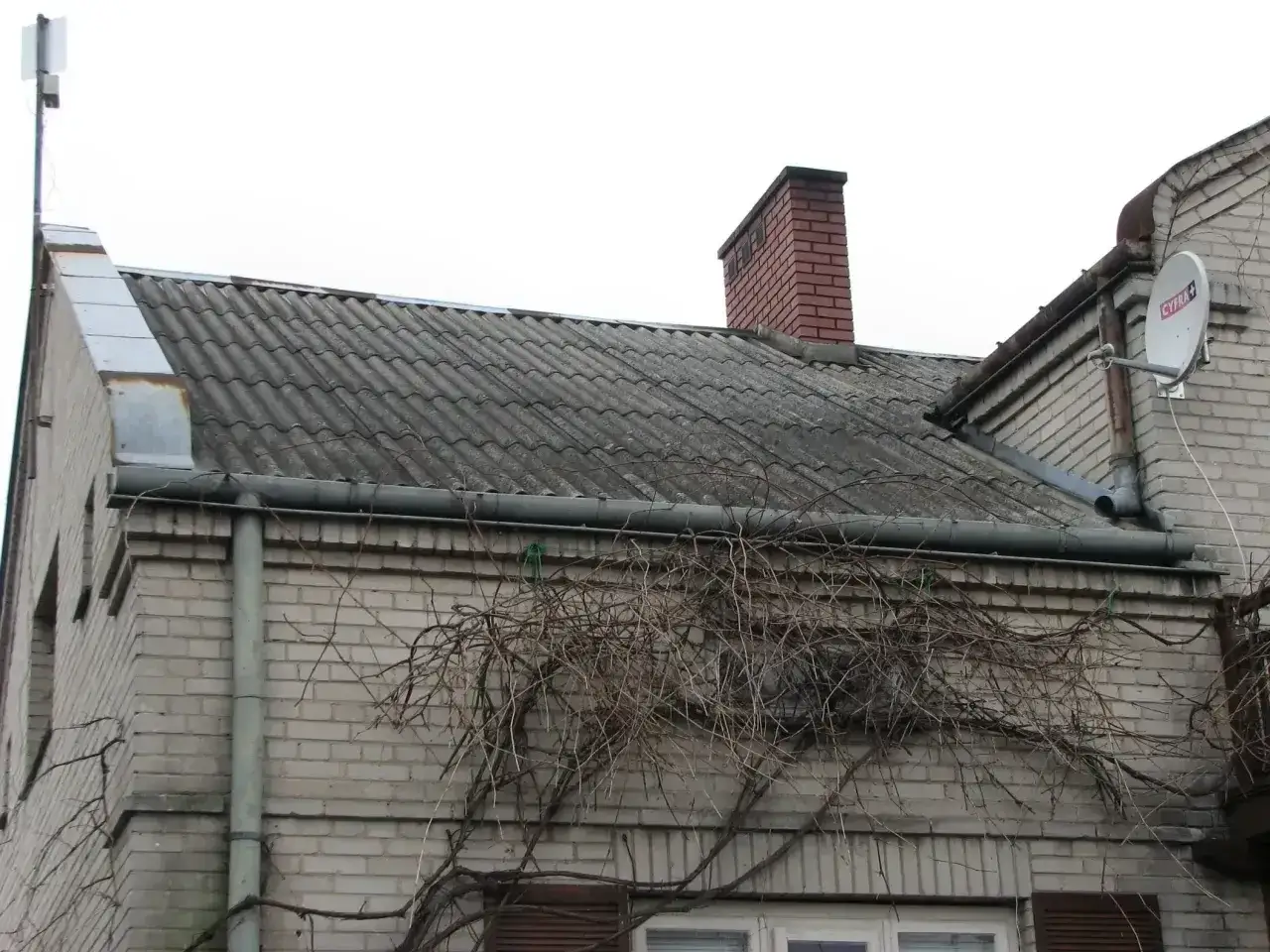 Dach pokryty eternitem, czyli materiałem zawierającym azbest, z kominem i anteną satelitarną.