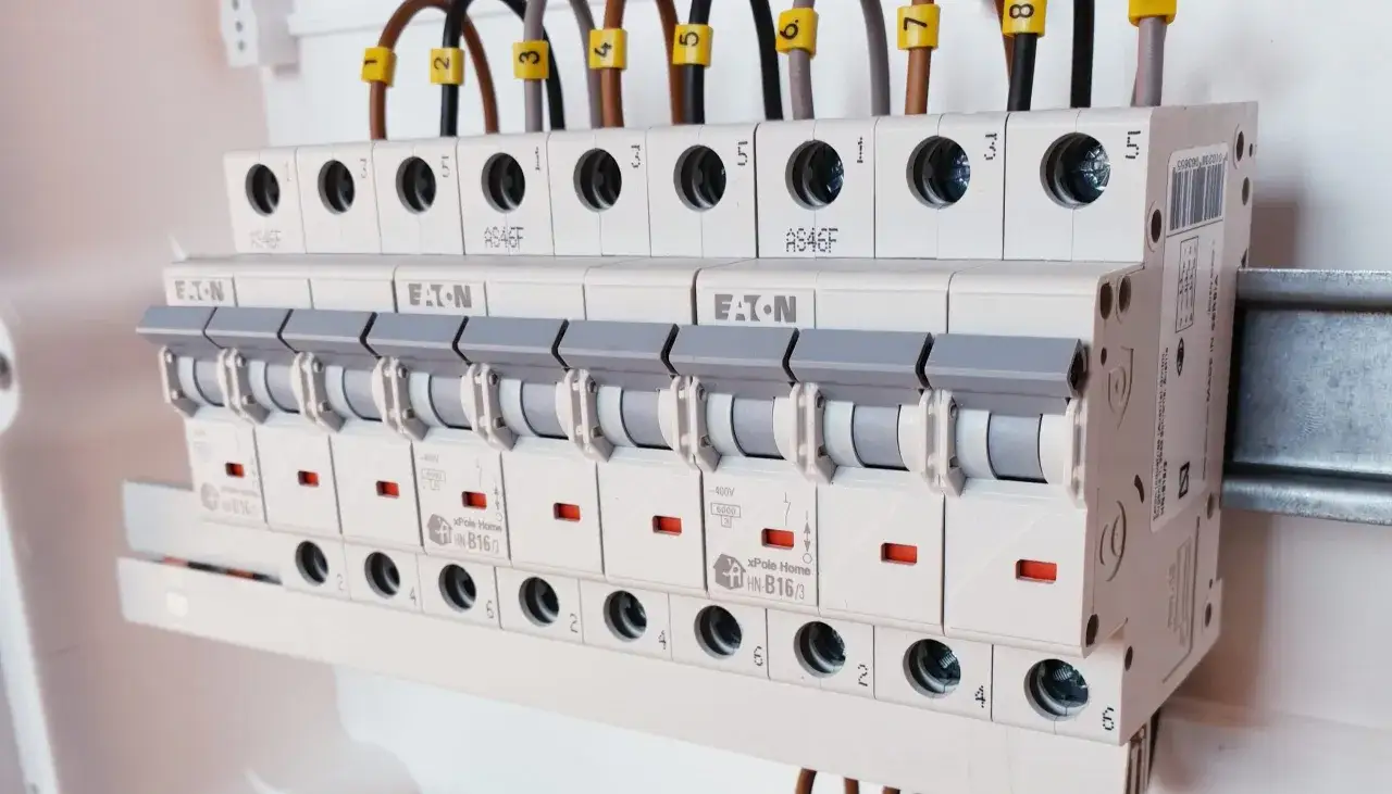 Różne rodzaje bezpieczników w rozdzielnicy elektrycznej, z widocznymi oznaczeniami i przewodami.